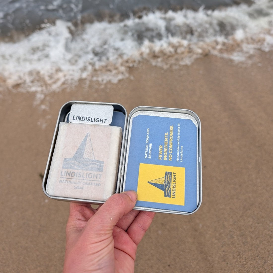 Lindislight travel tin open on sand, showing soap and balm tins inside