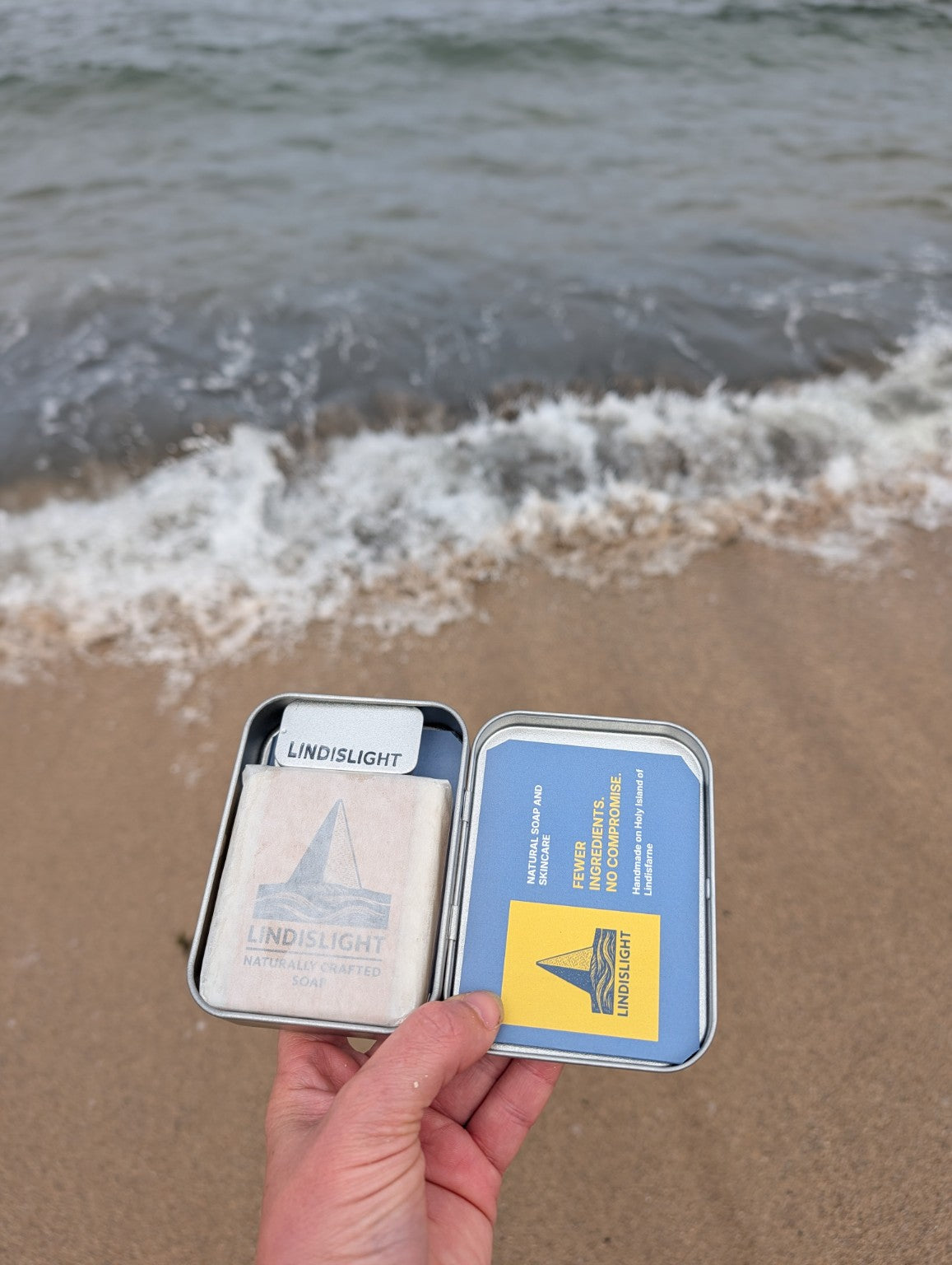 Lindislight tin open on the beach showing soap and ingredients guide